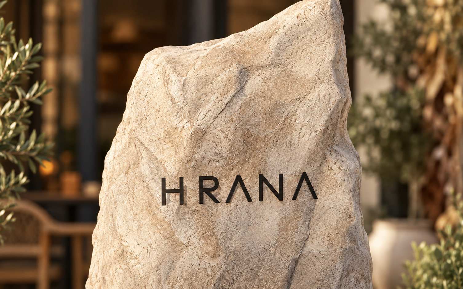 Piatra cu logo-ul HRANA de la intrarea restaurantului, între măslini