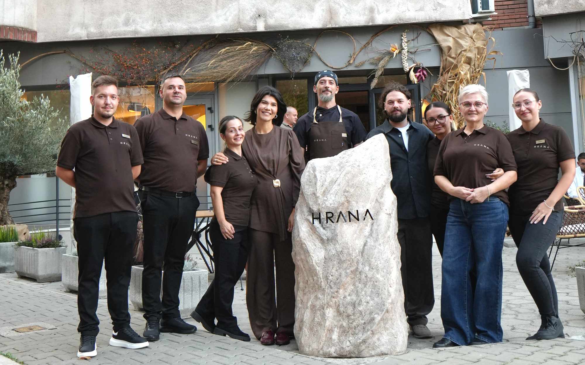 Echipa HRANA în fața pietrei cu logo de la intrarea restaurantului din Hunedoara